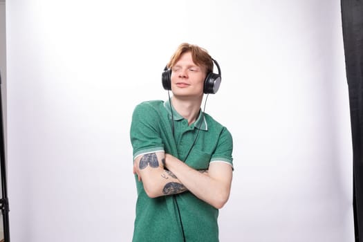 young handsome red-haired man in a green t-shirt enjoys and gets high from listening to music in headphones.