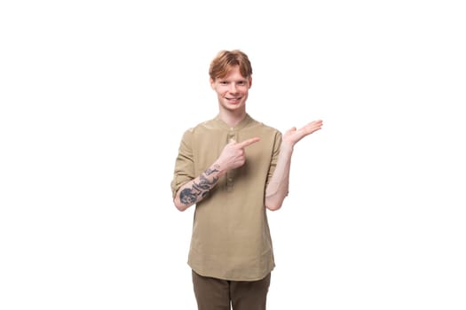 young surprised red-haired caucasian guy dressed in a khaki short sleeve shirt points to the side.