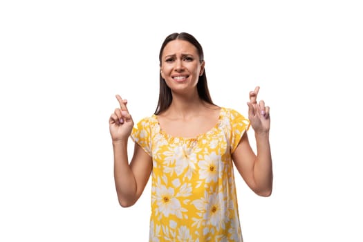 Caucasian young woman with straight black hair dressed in a yellow sundress crossed her fingers in hope and expectation.