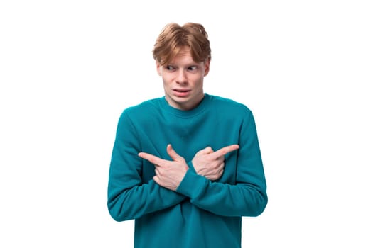 young handsome red-haired man with a blue sweater points his finger at the advertising space.