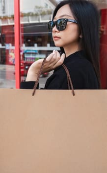 Side view of young Asian woman holding shopping bags on Black Friday while standing in the mall area copy space.
