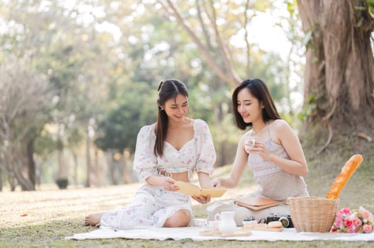 Two beautiful LGBT young women in casual clothes and summer hats Carefree woman having a picnic outside Positive model sitting on the grass eat fruit and cheese Take a selfie. LGBT concept.