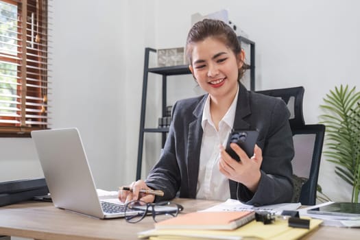 Businesswoman talking on business phone and using laptop to do finance, mathematics on wooden table in office and business background, tax, accounting, statistics and analytical research concepts..