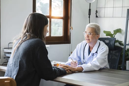 Elderly female doctor in white coat talking with beautiful young patient in clinic, giving advice on heart disease treatment and health care and medicine, medicine concept.