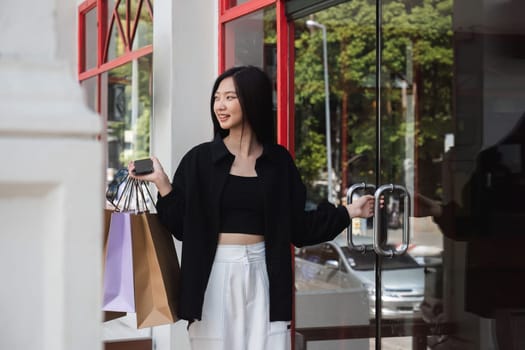 Asian woman using smartphone and looking away while enjoying a day shopping. Black Friday sale and discount. Buying clothes presents for holidays.