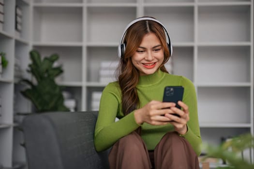 Happy Asian woman listening to music on mobile phone while sitting on sofa at home Relaxed smiling girl with headphones in the morning It's time to rest..