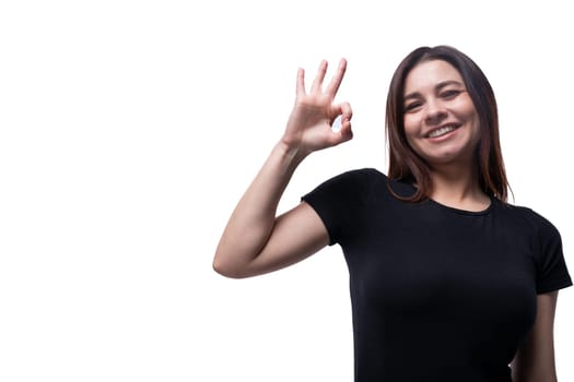 Caucasian cute young woman with black hair dressed in a black t-shirt gesturing on a white background with copy space.