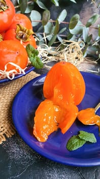 Persimmon on a dark background. Fresh, ripe fruits on a blue plate and in a box. Healthy eating.