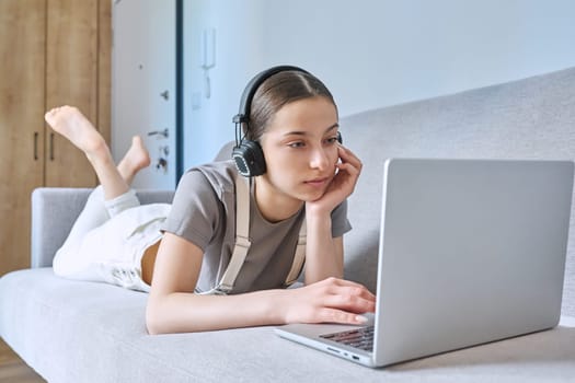 Teen girl in headphones at home on couch, looking at laptop webcam, typing having video chat call conference. Technology for learning leisure study communication modern lifestyle adolescence concept