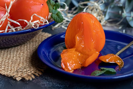 Persimmon on a dark background. Fresh, ripe fruits on a blue plate and in a box. Healthy eating.