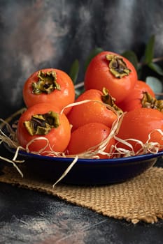 Persimmon on a dark background. Fresh, ripe fruits on a blue plate and in a box. Healthy eating.