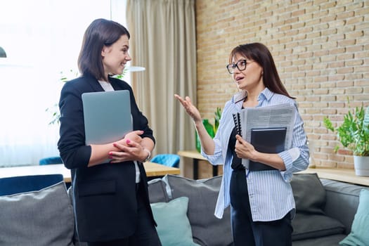 Two businesswomen talking and discussing in office. Female colleagues, manager and employee analyze and discuss documents, contracts, financial reports. Work law finance teamwork people job concept