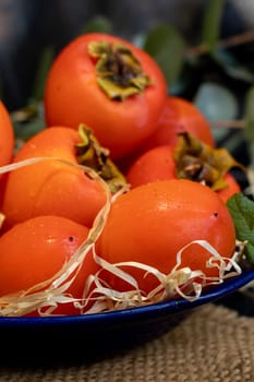 Persimmon on a dark background. Fresh, ripe fruits on a blue plate and in a box. Healthy eating.