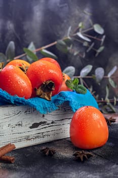 Persimmon on a dark background. Fresh, ripe fruits on a blue plate and in a box. Healthy eating.