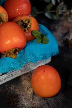 Persimmon on a dark background. Fresh, ripe fruits on a blue plate and in a box. Healthy eating.