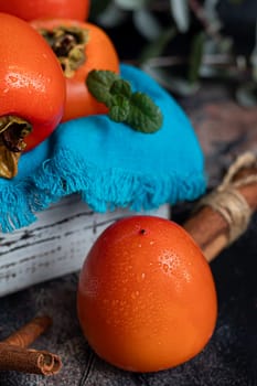 Persimmon on a dark background. Fresh, ripe fruits on a blue plate and in a box. Healthy eating.