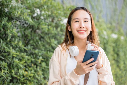 A happy and relaxed young woman is engrossed in her favorite energetic music using wireless headphones while dancing in the urban city garden. Her joyful expression enhances the season vibrancy.