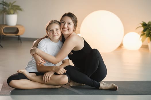 portrait of a mother and daughter of a teenager in sports clothes hugging, who are together in a fitness room. the concept of family sports.