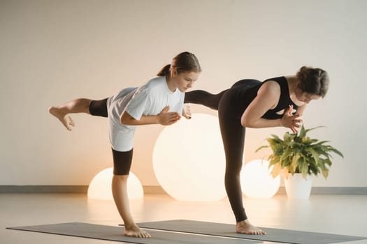 Mom and teenage daughter do gymnastics together in the fitness room. A woman and a girl train in the gym.