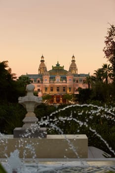 Monaco, Monte-Carlo, 12 November 2022: The famous square of Casino Monte-Carlo is at dusk, attraction night illumination, luxury cars, players, tourists, splashes of fountain. High quality photo