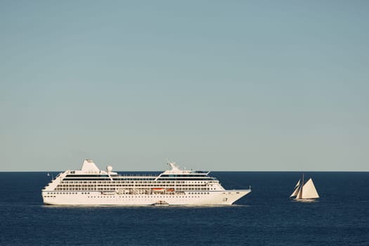 Monaco, vintage sail yacht and huge cruise liner are in sea at sunset, huge motor ship, wealth life of billionaires . High quality photo