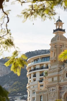 Monaco, Monte-Carlo, 21 October 2022: Towers of Casino Monte-Carlo at sunset, the famous hotel de Paris and mountain are on background, wealth life, famous landmark, pine trees, blue sky. High quality photo