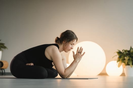 A girl in black sportswear does yoga on a mat in the fitness room.