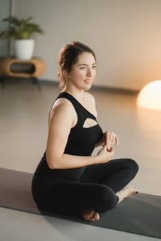 A girl in black sportswear does yoga on a mat in the fitness room.