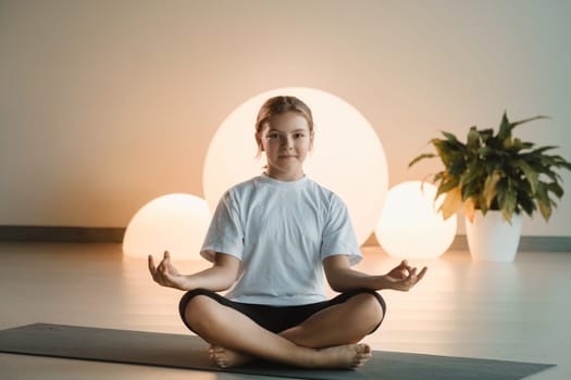 A teenage girl in sports clothes does yoga in a fitness room.