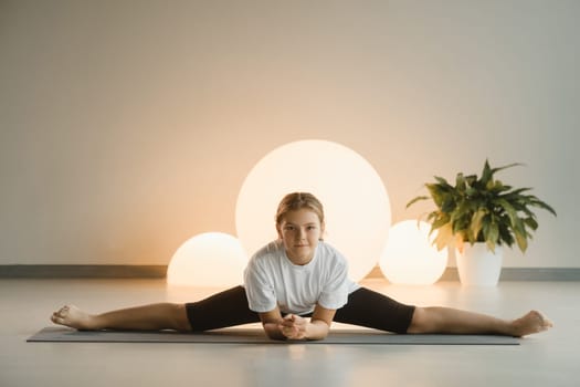 A teenage girl in sports clothes does yoga in a fitness room.