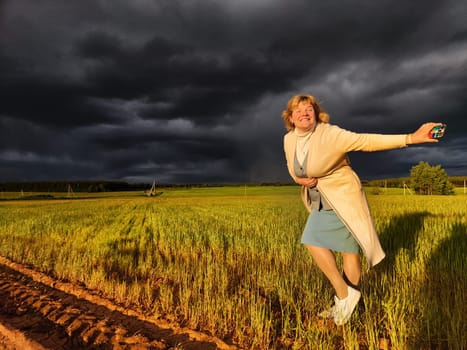 An adult girl in a field and with stormy sky with clouds posing for picture in the rain. A woman having fun outdoors on rural and rustic nature