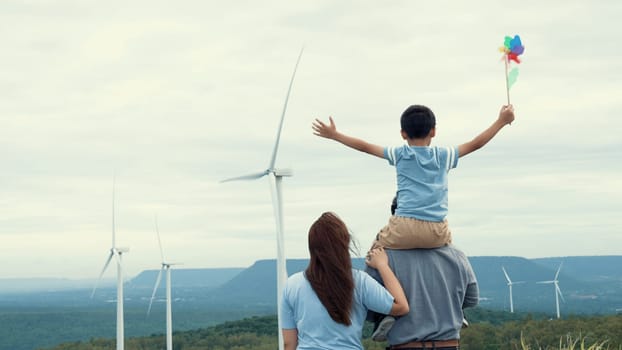 Concept of progressive happy family enjoying their time at the wind turbine farm. Electric generator from wind by wind turbine generator on the country side with hill and mountain on the horizon.