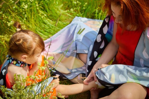 Happy female family with mother and daughter on green and yellow meadow full of grass and flower. Woman with red hair and blonde girl having fun, joy and hug in sunny summer day. Concept family love