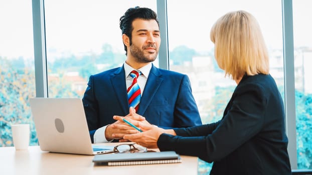 Two business people talk project strategy at office meeting room. Businessman discuss project planning with colleague at modern workplace while having conversation and advice on financial report. Jivy