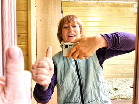 Middle-aged woman using smartphone for selfie and blogging. Female blogger poses in a photo. The girl admires herself in the mirror