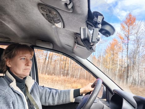 Portrait of female driver in solo journey. Adult mature woman holding steering wheel and looking through windscreen in travel by vehicle on vacation. Lady girl who is owner or rent car for travel