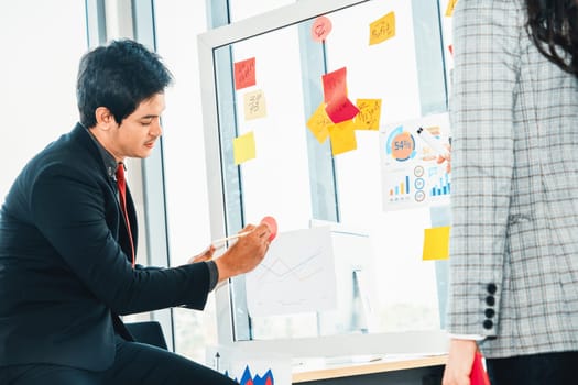 Business people work on project planning board in office and having conversation with coworker friend to analyze project development . They use sticky notes posted on glass to make it organized. Jivy