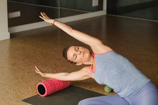 Slender girl doing yoga with a big massage roller on the floor.