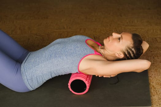 Slender girl doing yoga with a big massage roller on the floor.