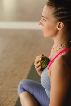 A woman does self - massage with a small ball while sitting in a fitness room . Myofascial relaxation.