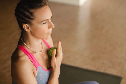 A woman does self - massage with a small ball while sitting in a fitness room . Myofascial relaxation.