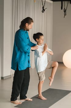 A yoga instructor in training helps a child to do exercises in the gym.