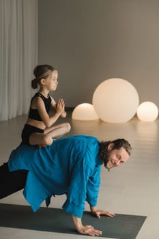 a child in the lotus position sits on the back of a yoga coach during training.