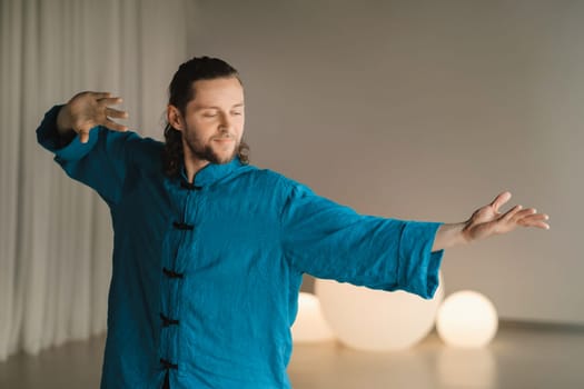 A man in a blue kimono does yoga indoors. Healthy lifestyle.