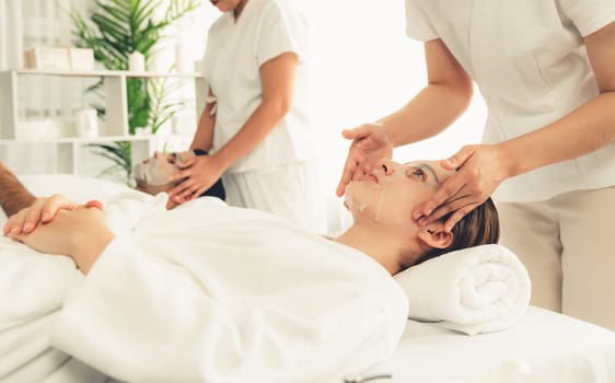 Serene modern daylight ambiance of spa salon, couple customer indulges in rejuvenating with facial skincare mask. Facial skin treatment and beauty cosmetology procedure for face. Quiescent