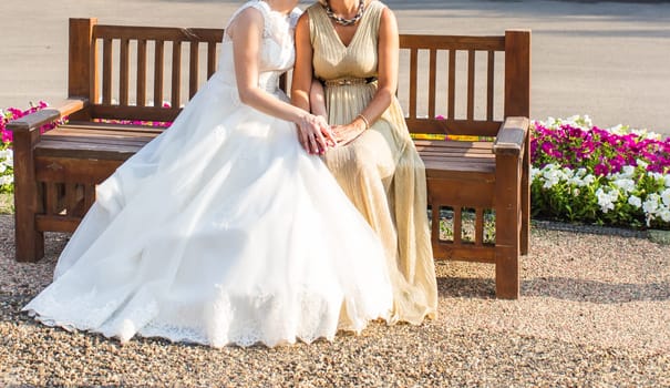 Bride With Mother sitting on a bench outdoors.