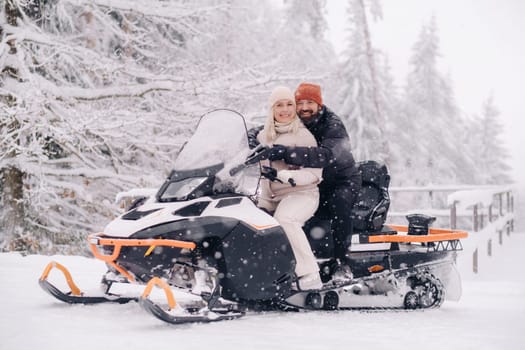 A couple, a man and a woman, on a snowmobile in a winter forest.