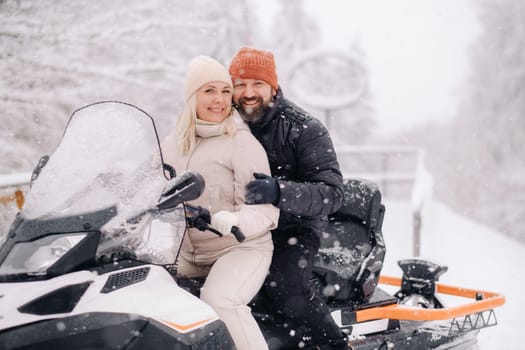 A couple, a man and a woman, on a snowmobile in a winter forest.