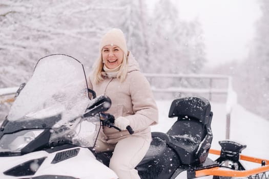 A cheerful woman rides a snowmobile in a winter forest.