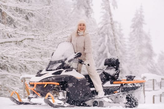 A cheerful woman rides a snowmobile in a winter forest.